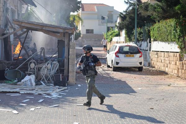 A member of the Israeli forces runs past a fire rages in a house in Ashkelon, following a Hamas rocket attack from the Gaza Strip on southern Israel on Oct. 7, 2023.